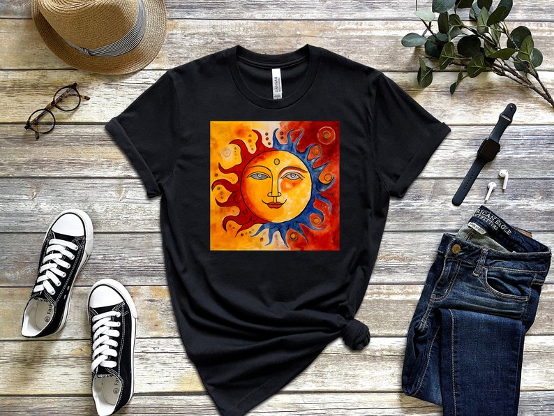 May include: Black t-shirt featuring a colourful sun illustration with a face, set against a yellow background with blue and red accents.