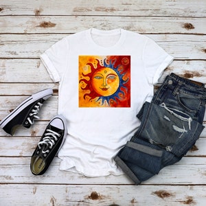 May include: White t-shirt featuring a colourful sun graphic. The sun has a face with blue eyes, a red nose, and a yellow smile. The sun is surrounded by orange and red flames.