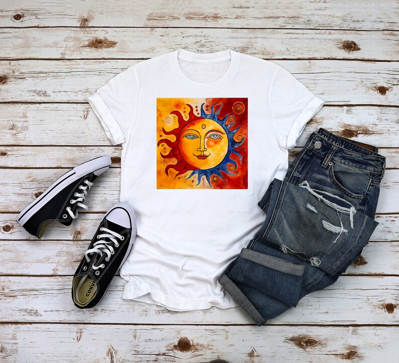 May include: White t-shirt featuring a colourful sun graphic. The sun has a face with blue eyes, a red nose, and a yellow smile. The sun is surrounded by orange and red flames.