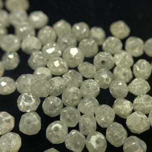 May include: A collection of small, faceted, translucent beads. The beads are irregularly shaped and have a slightly yellowish hue. They are scattered across a dark surface, creating a sparkling effect.