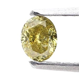 Puede incluir: Un diamante amarillo de corte ovalado sostenido por unas pinzas de metal plateado. La piedra preciosa presenta una superficie facetada que refleja la luz, mostrando un tono amarillo vibrante y saturado en toda su estructura interna.