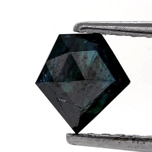 Könnte beinhalten: Ein fünfeckiger loser Edelstein mit einer tiefdunkelblauen und schwarzen Farbpalette. Der Stein weist eine facettierte Oberfläche mit geometrischen Dreiecks- und Rauten-Schliffen auf, die das Licht reflektieren, gehalten von einer Metallpinzette.