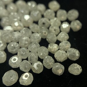 May include: A collection of small, faceted, clear beads with a slightly iridescent sheen. The beads are irregularly shaped and appear to be made of a translucent material, possibly glass or crystal. They are scattered against a dark background.