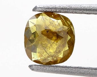 May include: A faceted, oval-shaped yellow gemstone held by a pair of silver tweezers. The gem has a warm, golden hue with multiple facets that reflect light. The background is plain white.