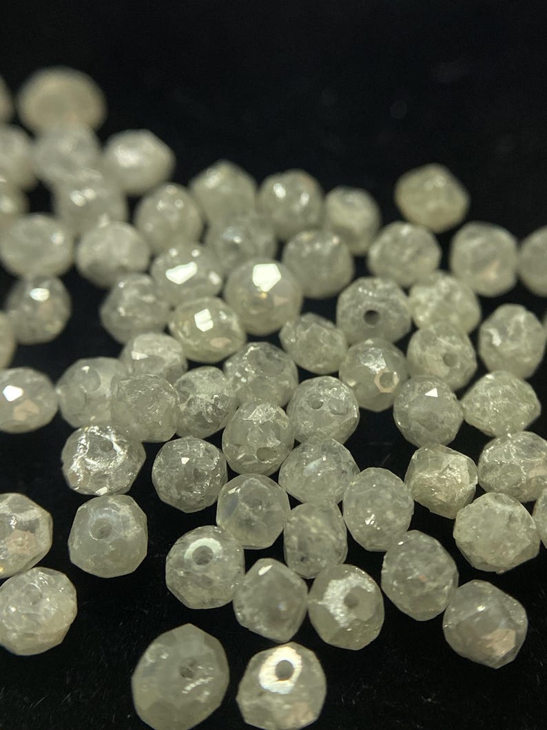 May include: A collection of small, faceted, translucent beads. The beads are irregularly shaped and have a slightly yellowish hue. They are scattered across a dark surface, creating a sparkling effect.