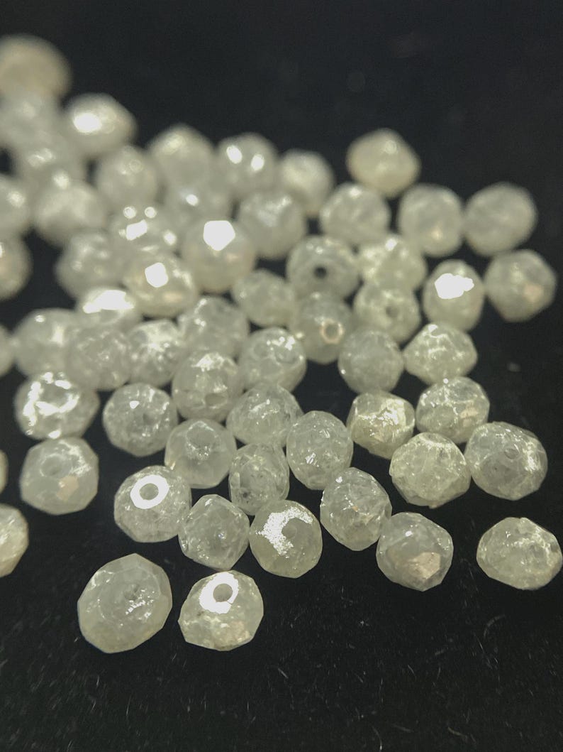 May include: A collection of small, irregularly shaped, clear beads with a faceted surface. The beads are scattered across a dark surface, catching the light and creating a sparkling effect. These beads could be used for jewelry making or other crafts.