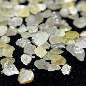 以下が含まれることがあります： さまざまな形とサイズの未加工ダイヤモンドのコレクション。 ダイヤモンドは、透明、淡い黄色、オフホワイトなど、さまざまな色を示し、きらびやかで半透明な外観をしています。 宝石は暗い表面に散らばっています。