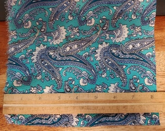May include: A turquoise fabric with a paisley pattern in shades of blue and white. The fabric is measured with a ruler, showing it is 8 inches wide.
