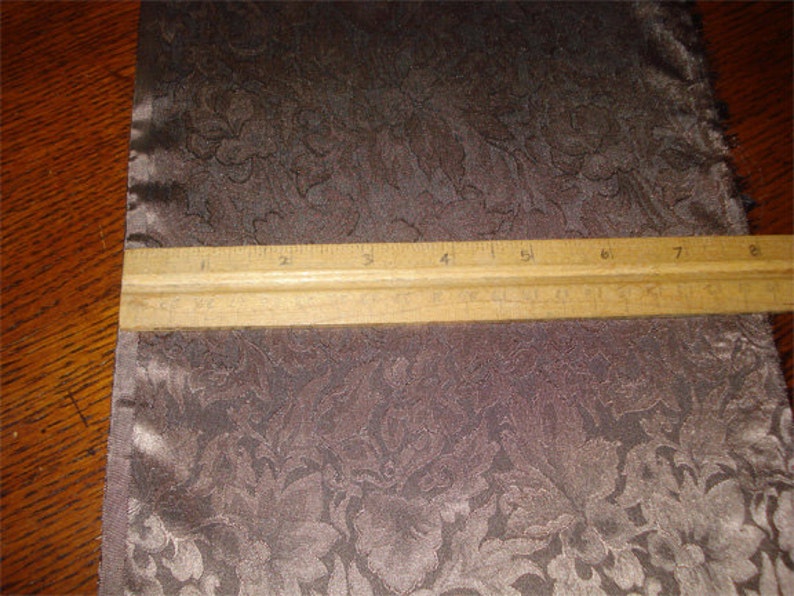 K&ouml;nnte beinhalten: Nahaufnahme eines braunen Stoffes mit einem Blumenmuster. Ein Lineal liegt auf dem Stoff und zeigt eine Messung von 20,3 cm.