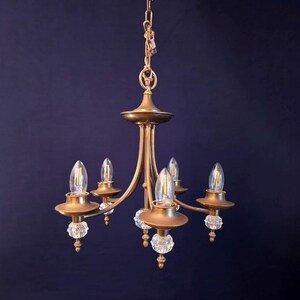 May include: A vintage brass chandelier with five lights. The fixture has a central column with curved arms extending outwards, each holding a light bulb. Clear crystal ball accents are visible. The chandelier hangs from a chain.