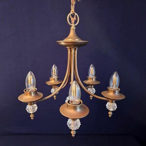 May include: A vintage brass chandelier with five light fixtures. Each fixture has a clear, teardrop-shaped bulb and is accented with a crystal ball. The chandelier is suspended from a chain.