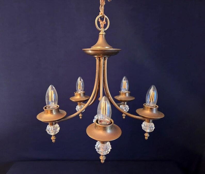 May include: A vintage brass chandelier with five light fixtures. Each fixture has a clear, teardrop-shaped bulb and is accented with a crystal ball. The chandelier is suspended from a chain.