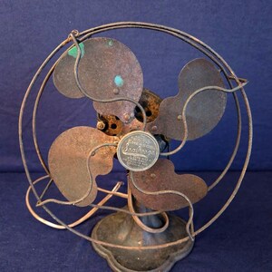 Peut inclure: Un ancien ventilateur Emerson Seabreeze avec une cage circulaire et quatre pales. Le ventilateur pr&eacute;sente un aspect rouill&eacute; et vieilli, avec une base en m&eacute;tal et un petit embl&egrave;me circulaire au centre. Objet de d&eacute;coration vintage.