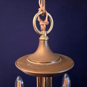 May include: Close-up of a vintage brass chandelier. The fixture features a circular top, a decorative ring, and a rope for hanging. The brass has a warm, aged patina, and the design suggests a classic or antique style.