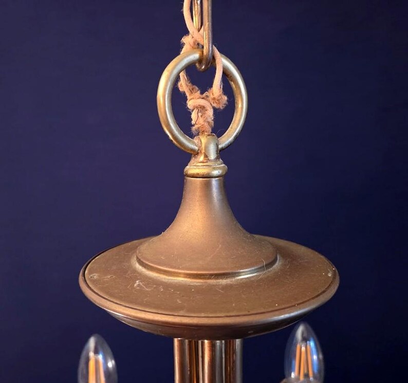 May include: Close-up of a vintage brass chandelier. The fixture features a circular top, a decorative ring, and a rope for hanging. The brass has a warm, aged patina, and the design suggests a classic or antique style.