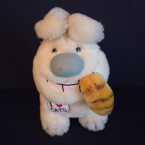 May include: A plush white cat-like toy with a blue nose and a smiling face. It has two fluffy ears and a paw with orange and yellow stripes. A heart-shaped tag reads "I ❤️ CATS".