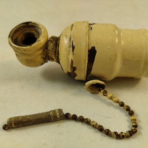 May include: A vintage off-white light fixture socket with a pull chain. The chain has a wooden pull and brown and white beads.