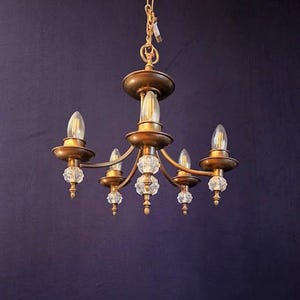 May include: A vintage-style chandelier with a gold finish and five light fixtures. The chandelier features clear crystal accents and is suspended from a gold chain. The bulbs are elongated and clear, providing a warm glow.