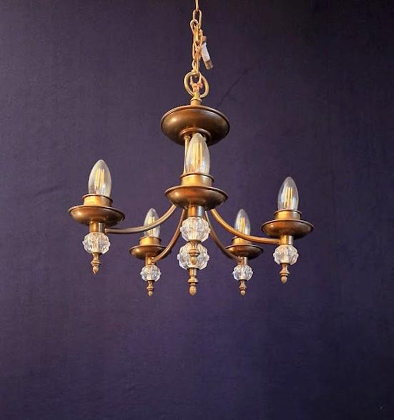 May include: A vintage-style chandelier with a gold finish and five light fixtures. The chandelier features clear crystal accents and is suspended from a gold chain. The bulbs are elongated and clear, providing a warm glow.