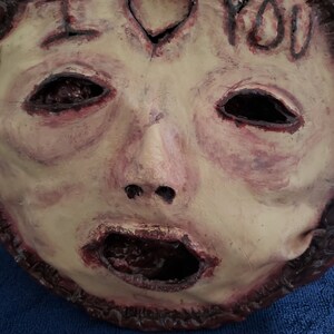 May include: A creepy, pale-skinned mask with a gaping mouth and hollow eyes. The mask has a heart with the words "I love you" written on it.