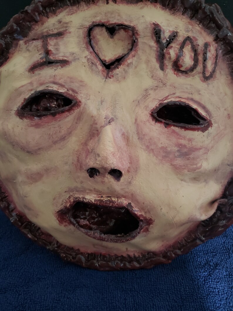 May include: A creepy, pale-skinned mask with a gaping mouth and hollow eyes. The mask has a heart with the words "I love you" written on it.