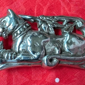 May include: Silver tone brooch featuring a detailed sculpted cat design. The cat is sitting on a branch with leaves and flowers.