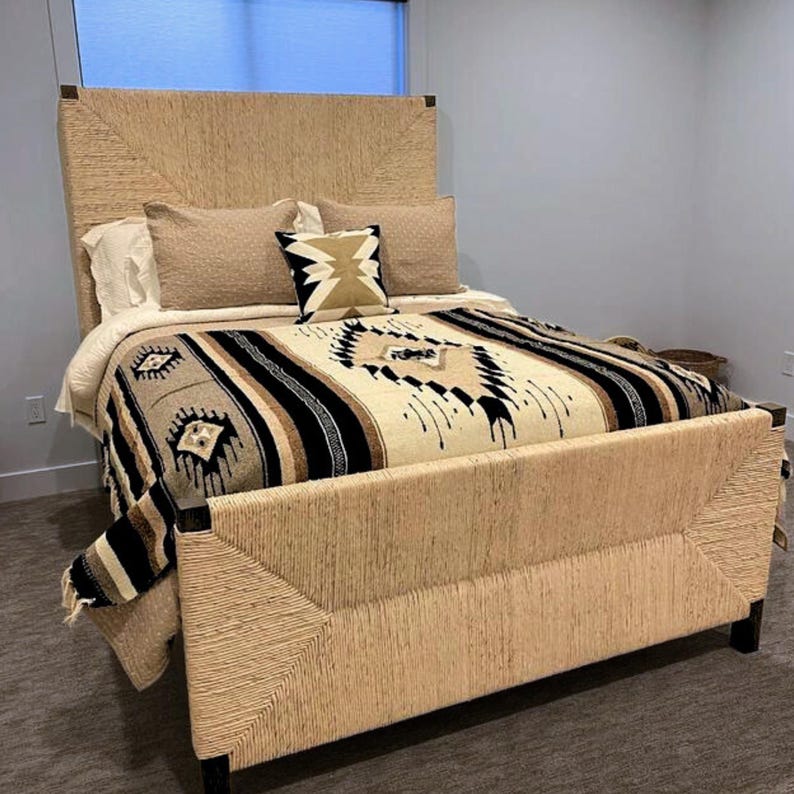 May include: A bed with a woven headboard and footboard, featuring a cream and black patterned blanket and a brown throw pillow with a geometric design.