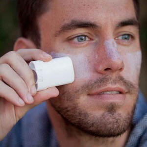 May include: A person applying white sunscreen to their face with a white stick applicator.
