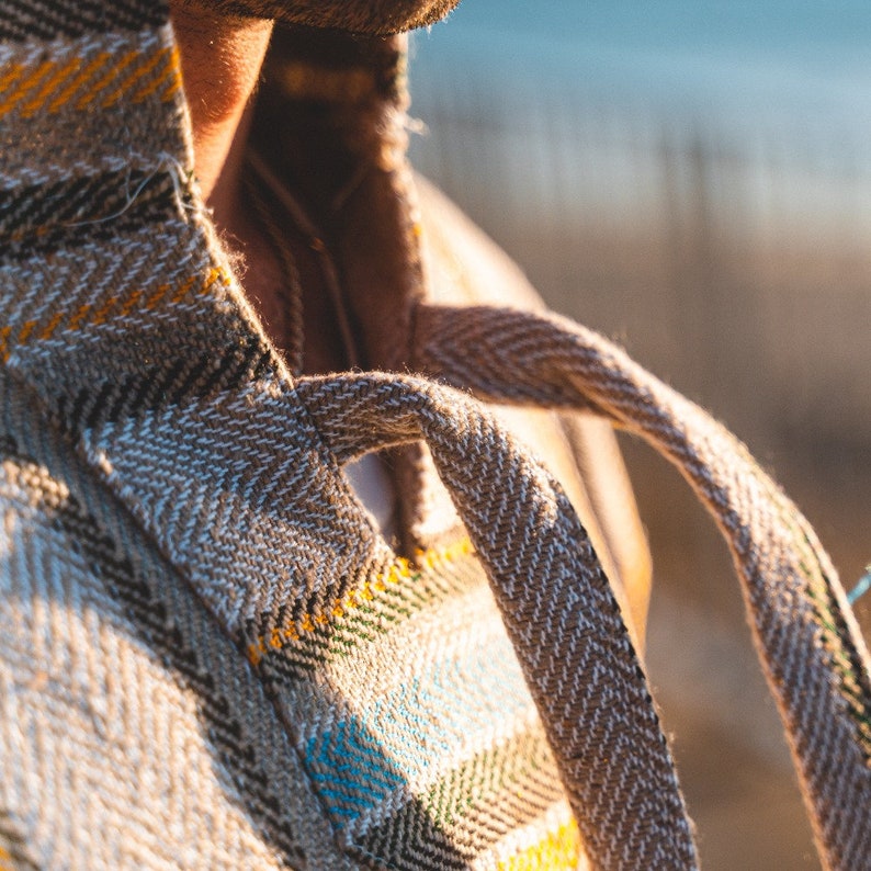 May include: Close-up of a beige and brown plaid tote bag with a herringbone weave. The bag has a sturdy handle made of the same material. Accents of yellow, black, and blue are visible in the plaid pattern.