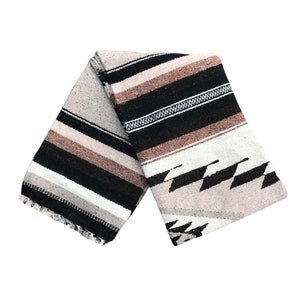 May include: A woven blanket with a striped pattern in shades of brown, black, and white. The blanket has a fringed edge and a geometric design on one side.