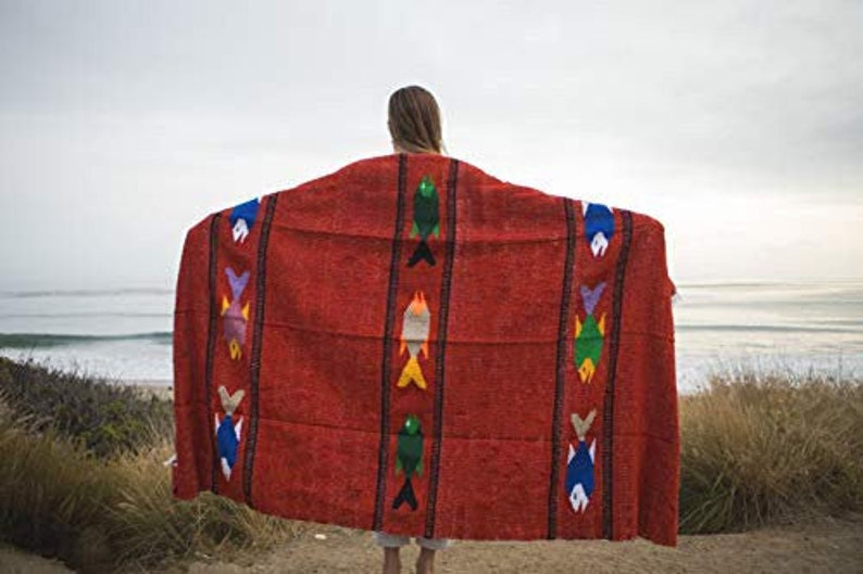 May include: A red woven blanket with colorful fish designs. The blanket is draped over a person's shoulders.