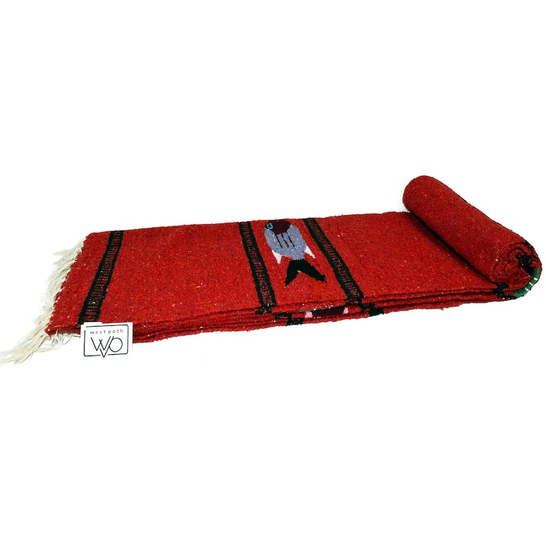 May include: Red woven Mexican blanket with a black and green fish design. The blanket is rolled up and has a tag that says "Westpath WO".