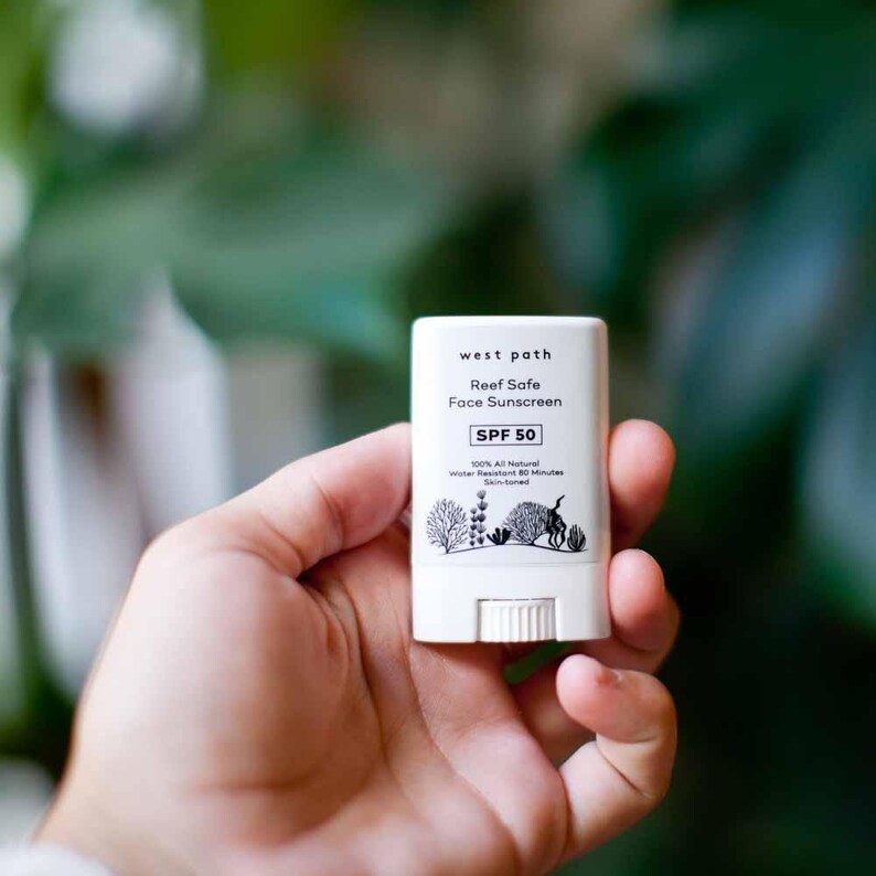 May include: A white sunscreen stick with black text that reads "west path Reef Safe Face Sunscreen SPF 50 100% All Natural Water Resistant 80 Minutes Skin-toned".
