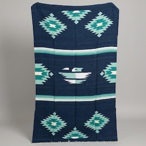 May include: A navy blue woven blanket with a geometric pattern in teal and white. The blanket features a central design of a stylized bird and horizontal stripes. The blanket is rectangular and has a fringed edge.