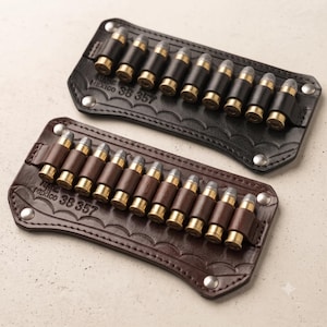 Könnte beinhalten: Zwei Patronenhalter aus Leder, einer in Schwarz und einer in Braun, mit jeweils neun Schlaufen für Munition mit Messinghülsen. Das Leder ist mit dem Text MADE IN MEXICO 38 357 geprägt und an den Ecken mit silberfarbenen Metallnieten versehen.