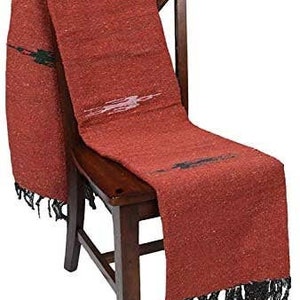 Pu&ograve; includere: Un tessuto tessuto color ruggine con frange nere e accenti decorativi neri e bianchi &egrave; drappeggiato su una sedia di legno. Il tessuto ha un aspetto strutturato ed &egrave; probabilmente una coperta o un plaid.