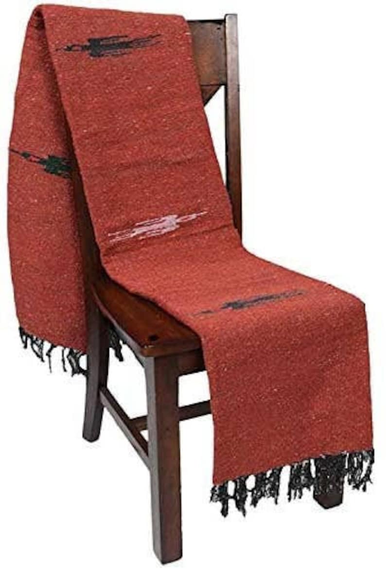 Pu&ograve; includere: Un tessuto tessuto color ruggine con frange nere e accenti decorativi neri e bianchi &egrave; drappeggiato su una sedia di legno. Il tessuto ha un aspetto strutturato ed &egrave; probabilmente una coperta o un plaid.