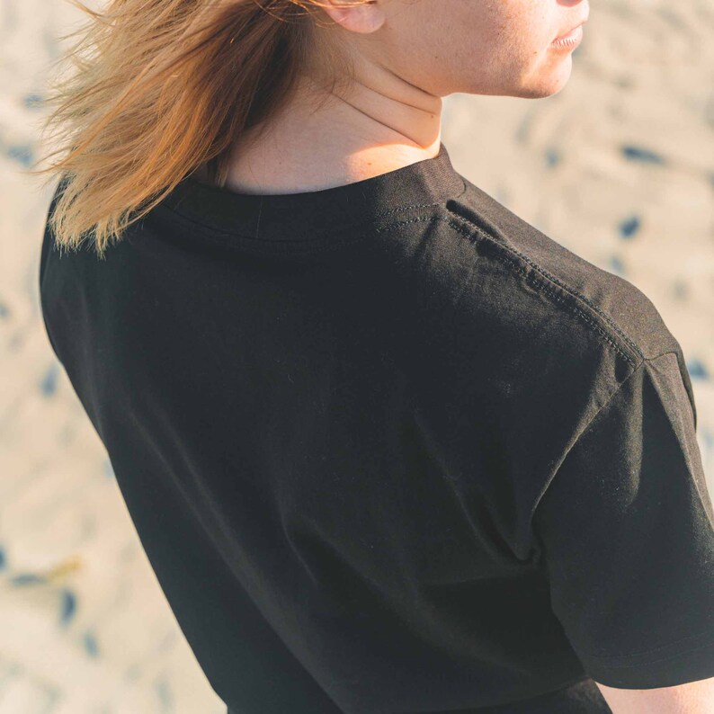 K&ouml;nnte beinhalten: Schwarzes Kurzarm-T-Shirt mit Rundhalsausschnitt. Der Stoff ist weich und blickdicht. Die Schulternaht ist sichtbar. Das Bild zeigt eine Nahaufnahme der R&uuml;ckseite des Shirts.
