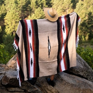 Könnte beinhalten: Eine Person trägt eine braun-weiß gestreifte Decke mit einem schwarz-weißen Rautenmuster. Die Decke ist über die Schultern der Person gelegt und sie trägt einen braunen Hut.