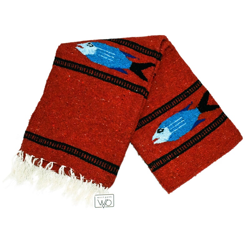 May include: Red Mexican blanket with a fringe border and two blue fish woven into the design. The blanket is folded in half and the brand label "Westfolk" is visible.