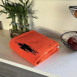 May include: A folded orange towel with a black silhouette of a person on it.