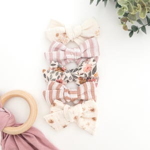 May include: Five fabric hair bows in a variety of patterns. The bows are stacked on top of each other. The bows are made of a soft, cotton fabric and are perfect for adding a touch of whimsy to any outfit.