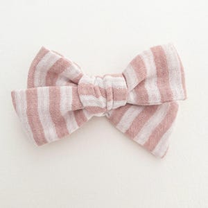 May include: A pink and white striped fabric bow. The bow is tied in a knot and has a soft, textured look.