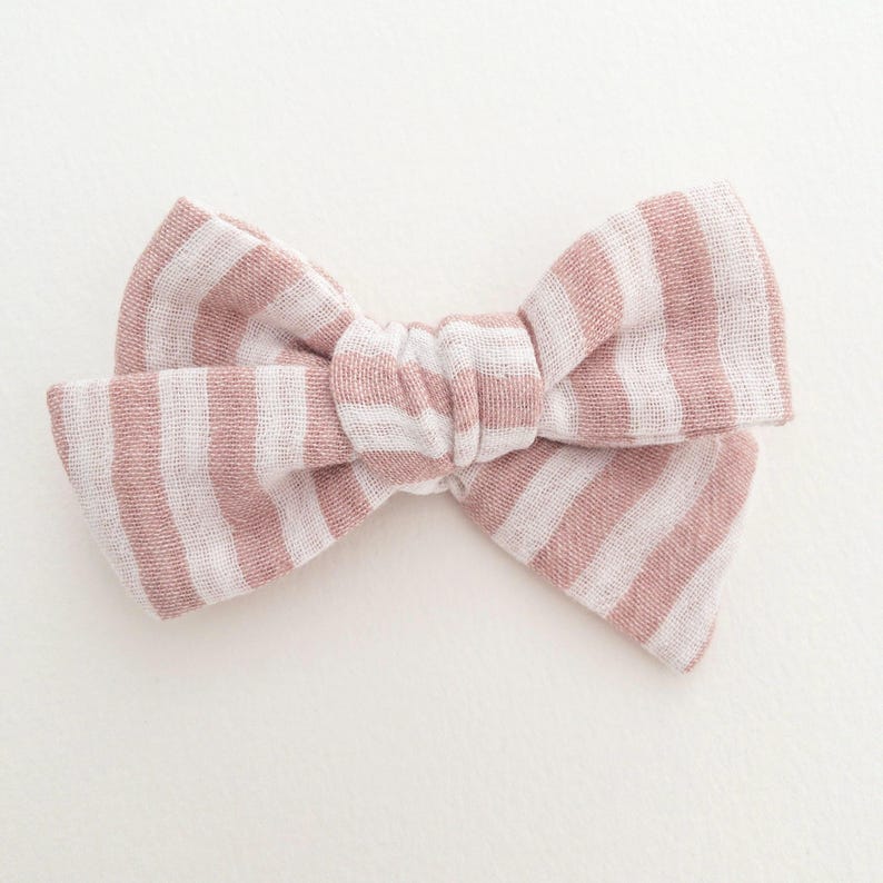May include: A pink and white striped fabric bow. The bow is tied in a knot and has a soft, textured look.