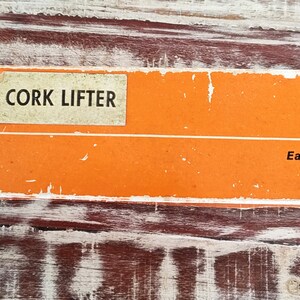May include: A vintage orange and white box with the text "CORK LIFTER" and "Easy Wine Cork Removal" printed on it. The box has the brand name "EMIDE" printed on the side.