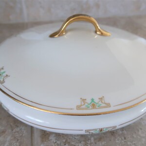 May include: White porcelain serving dish with a gold rim and green and gold floral design. The dish has two gold handles and a lid with a gold handle.