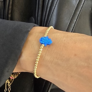 May include: A gold beaded bracelet with a blue hamsa charm. The bracelet is on a person's wrist.