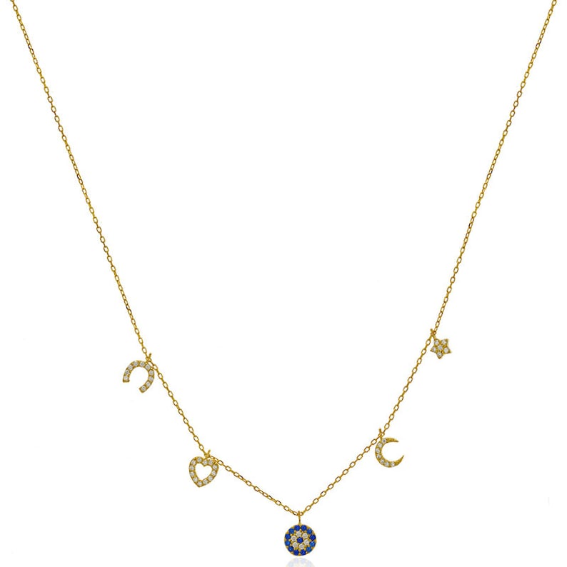 Puede incluir: Un collar de oro con un dije de ojo turco azul, una luna creciente, una herradura, un coraz&oacute;n y una estrella. Cada dije est&aacute; decorado con peque&ntilde;as piedras blancas.