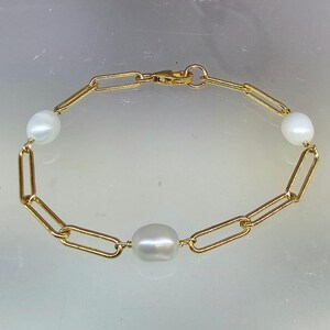 May include: A gold chain bracelet with three white oval pearls. The bracelet has a lobster clasp closure.
