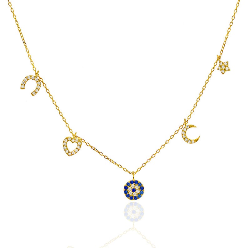 Puede incluir: Un collar de oro con una variedad de dijes, incluyendo una herradura, un coraz&oacute;n, una luna creciente, una estrella y un dije de ojo azul malvado. Los dijes est&aacute;n todos engastados con piedras de circonita c&uacute;bica transparentes.